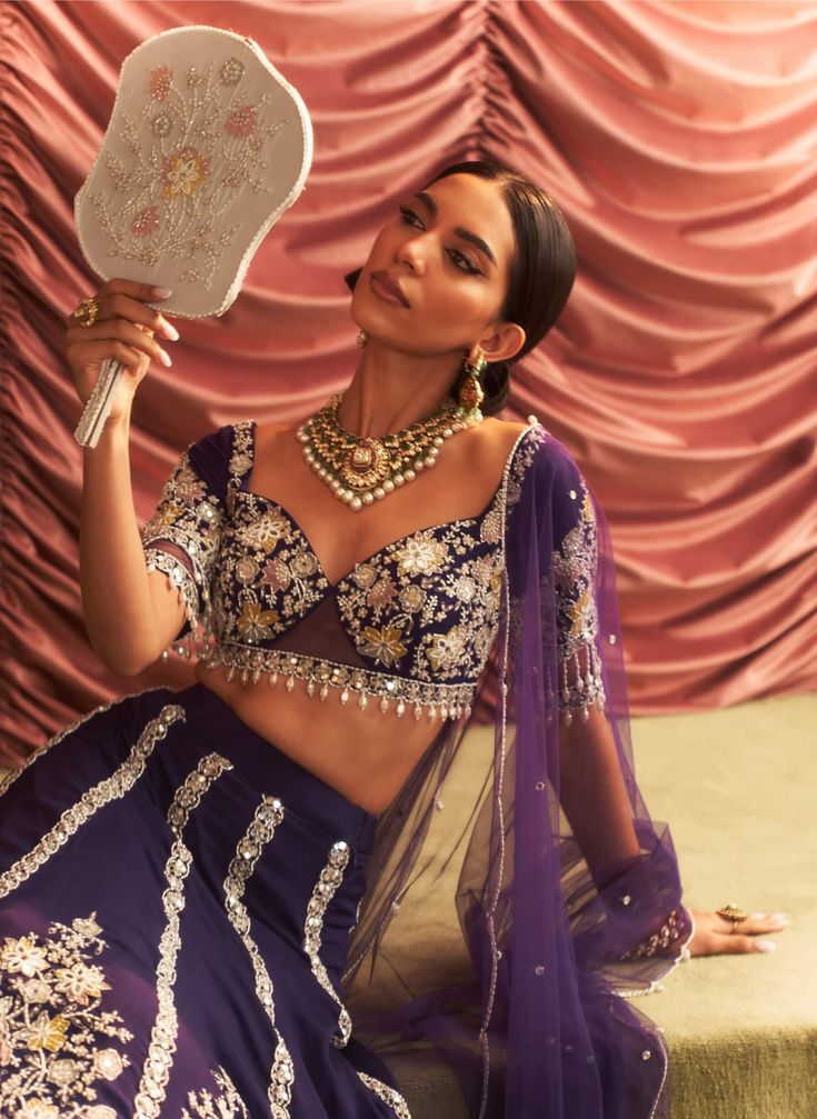 Make a grand entrance in this stunning purple embellished blouse, paired with a voluminous lehenga featuring cancan for added flair and drama. The matching dupatta completes the ensemble, creating a captivating look that is perfect for weddings and festive celebrations. Purple Sharara For Navratri With Traditional Drape, Purple Anarkali Style Sharara With Cutdana, Traditional Purple Sharara With Sheer Dupatta, Purple Sharara With Cutdana And Traditional Drape, Purple Sharara With Sheer Dupatta And Traditional Drape, Purple Sharara With Sheer Dupatta In Traditional Drape, Purple Sharara For Festivals With Traditional Drape, Purple Traditional Drape Sharara For Festivals, Purple Designer Wear Sets For Navratri