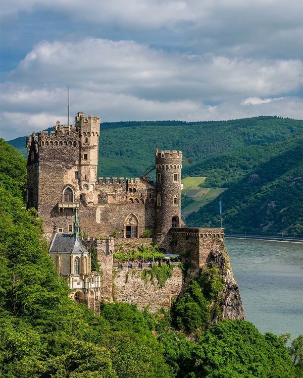 an old castle sitting on top of a cliff next to the water and mountains in the background