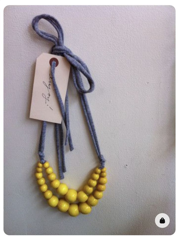 a yellow beaded necklace hangs on a gray cord with a white tag attached to it