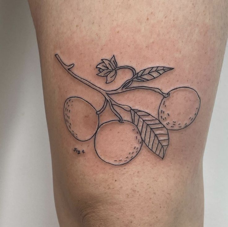 a tattoo on the leg of a woman with fruit and leaves in black ink,