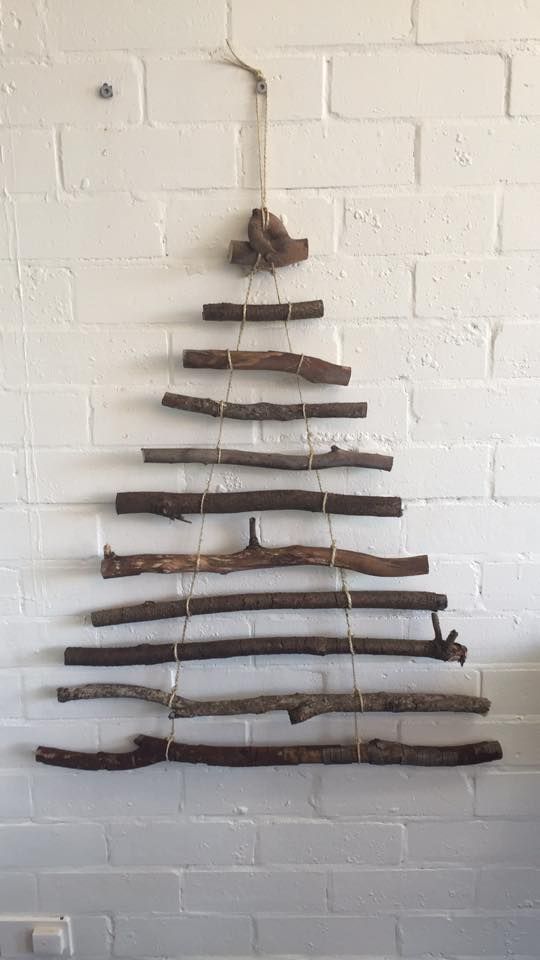 a christmas tree made out of driftwood hanging on a brick wall in front of a white brick wall