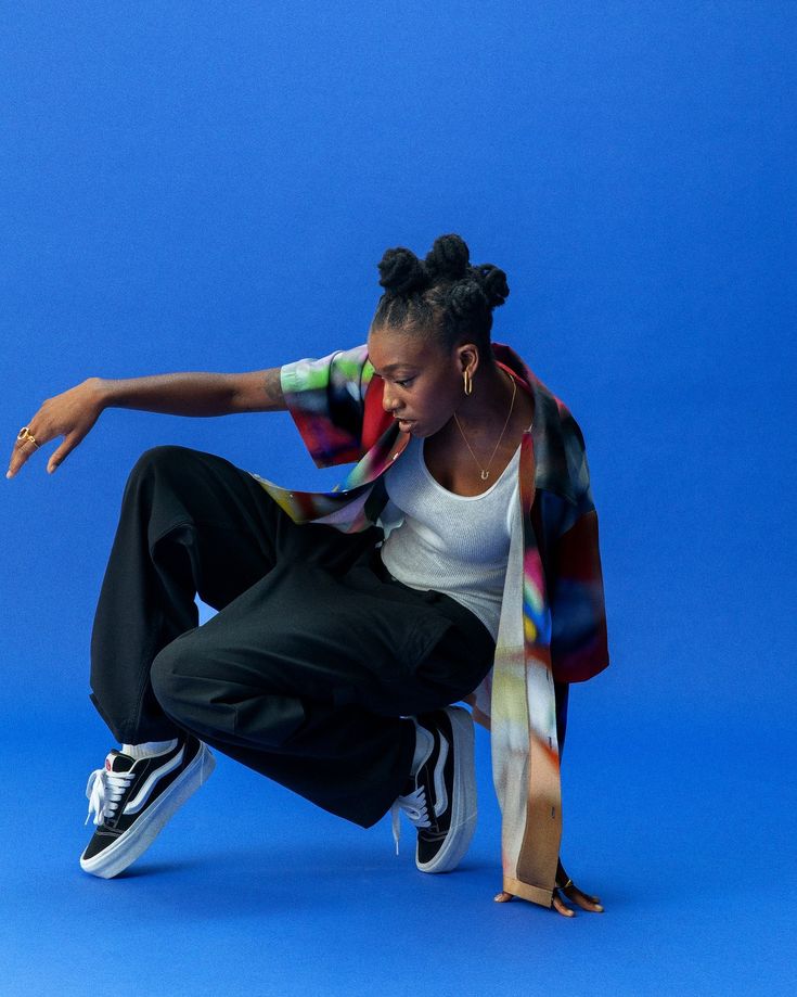 a woman in white shirt and black pants doing a trick on a skateboard against a blue background