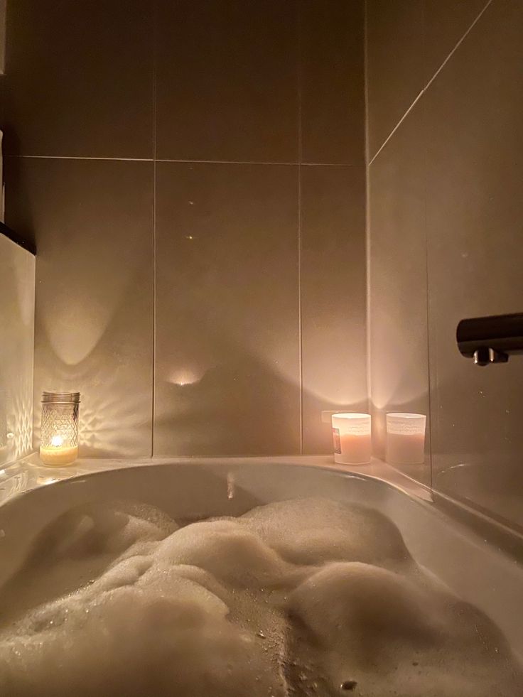 a bathtub filled with foam and water next to a lighted candle on the wall