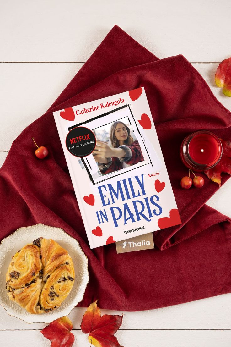 a book sitting on top of a red blanket next to a bowl of fruit and a candle