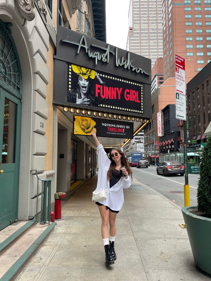 a woman holding up a funny sign on the side of a building in front of a theater