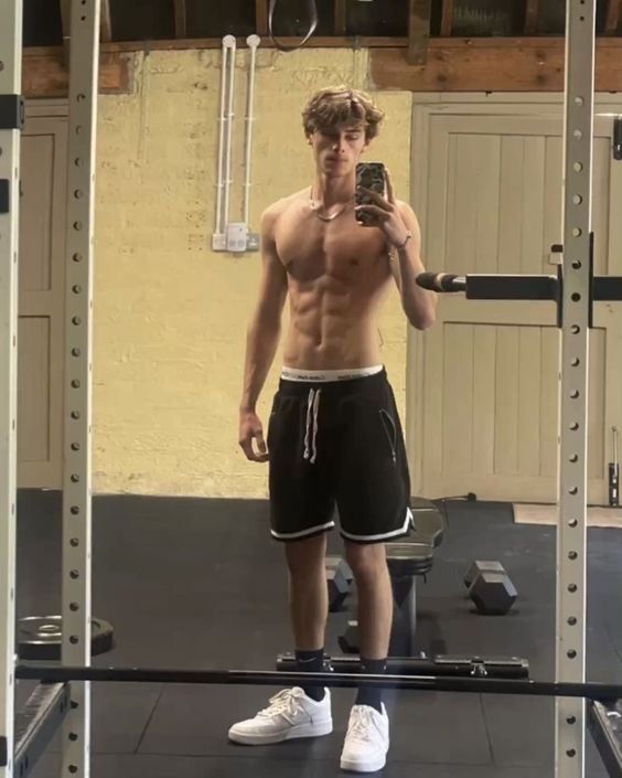 a shirtless man taking a selfie in the mirror with his cell phone while holding a barbell