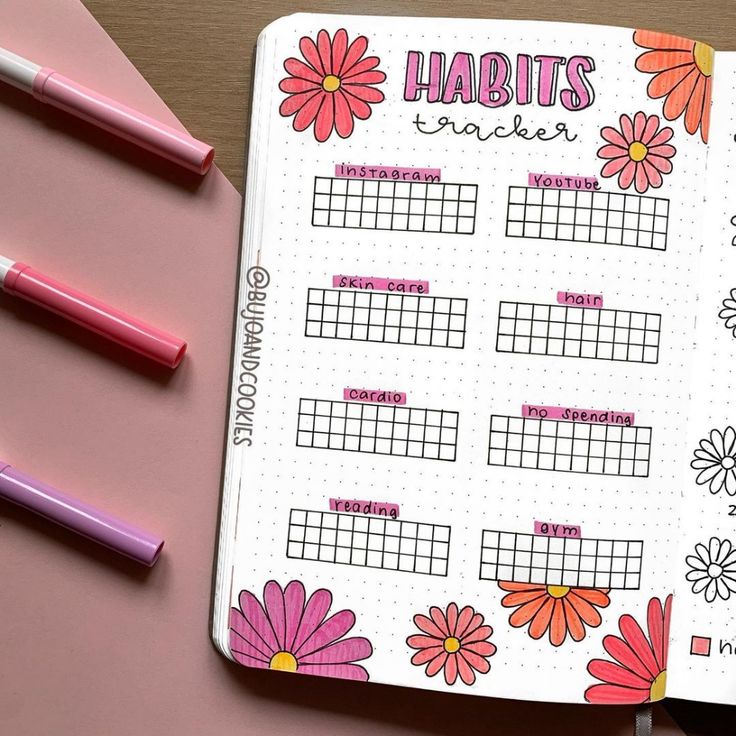 an open planner with flowers on it next to some pens and pencils in front of them