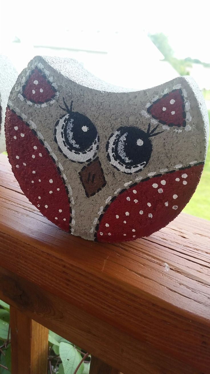 a rock with an owl face painted on it sitting on a wooden fence rail outside