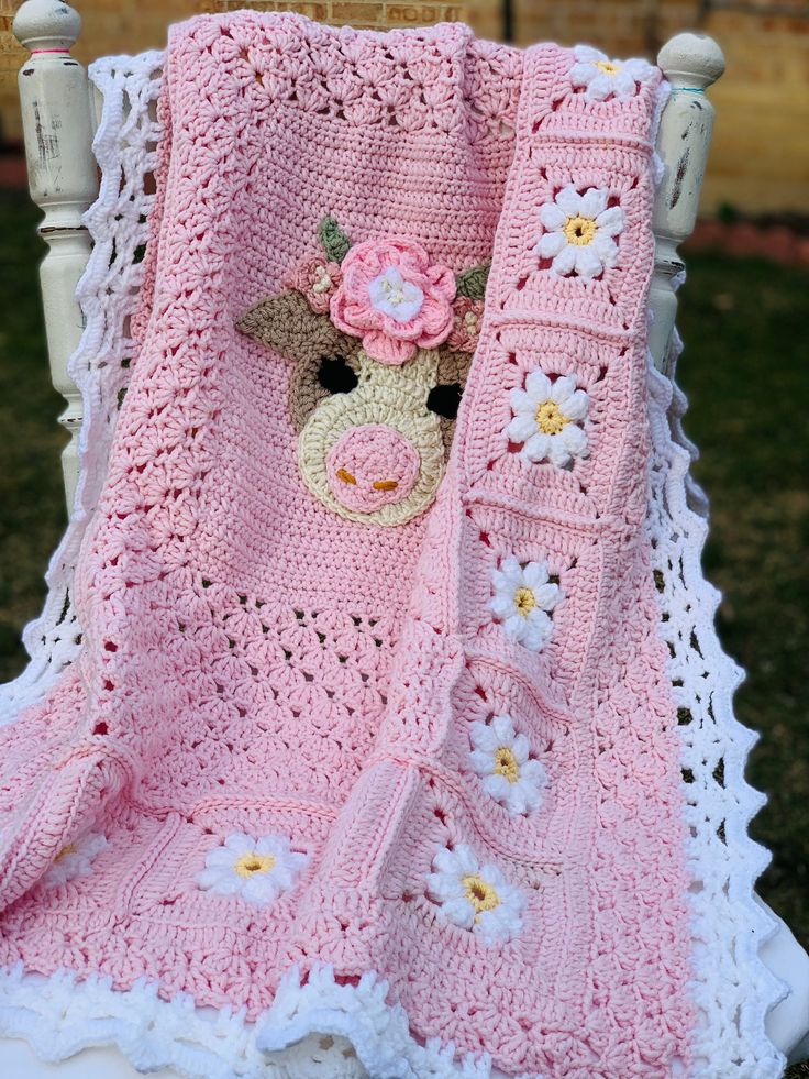 a crocheted blanket with a stuffed animal in the center and flowers on it