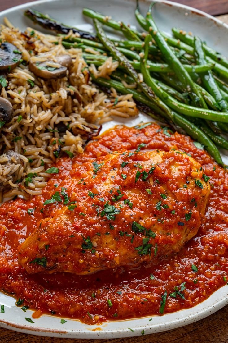 a white plate topped with meat covered in sauce next to green beans and rice on top of a wooden table