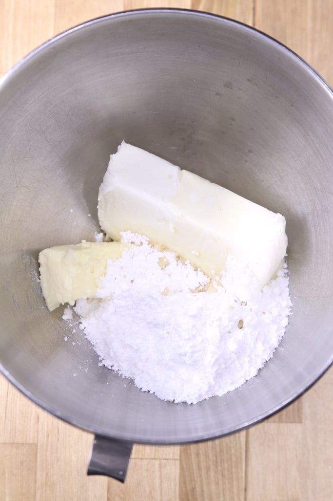 a metal bowl filled with sugar and butter on top of a wooden table next to a knife