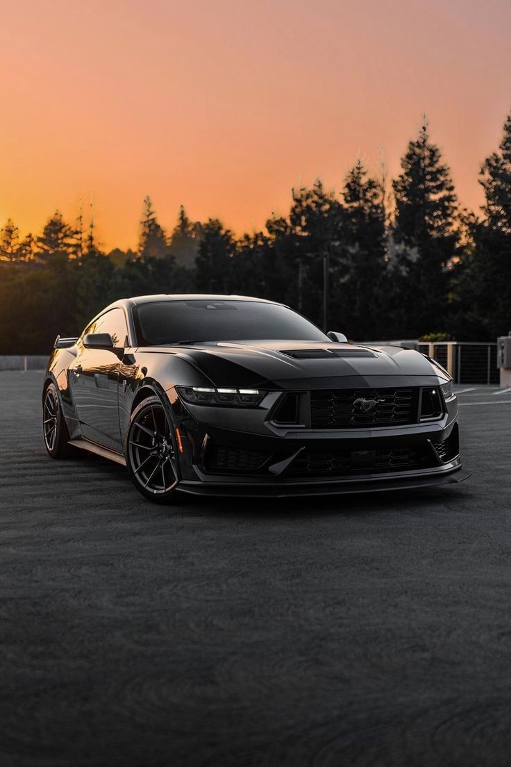 a black sports car parked in a parking lot with the sun setting on it's horizon