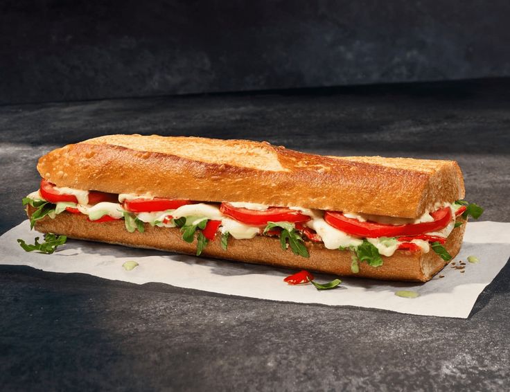 a sub sandwich with tomatoes, lettuce and mayonnaise on a piece of parchment paper