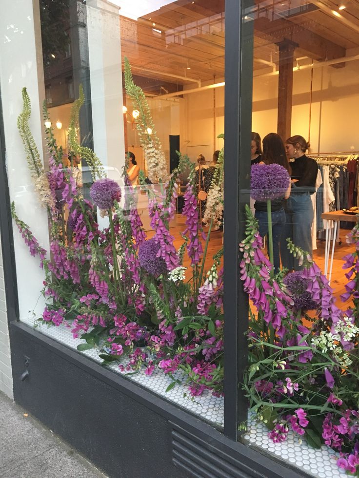 purple flowers in front of a window with people looking at them from inside the store