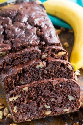 a loaf of chocolate banana bread sitting on top of a wooden cutting board next to two bananas