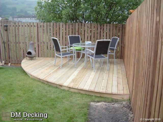 a wooden deck with table and chairs next to a fenced in area that has green grass