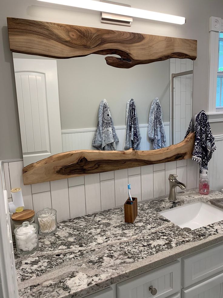 a bathroom with marble counter top and wooden mirror over the sink in front of it