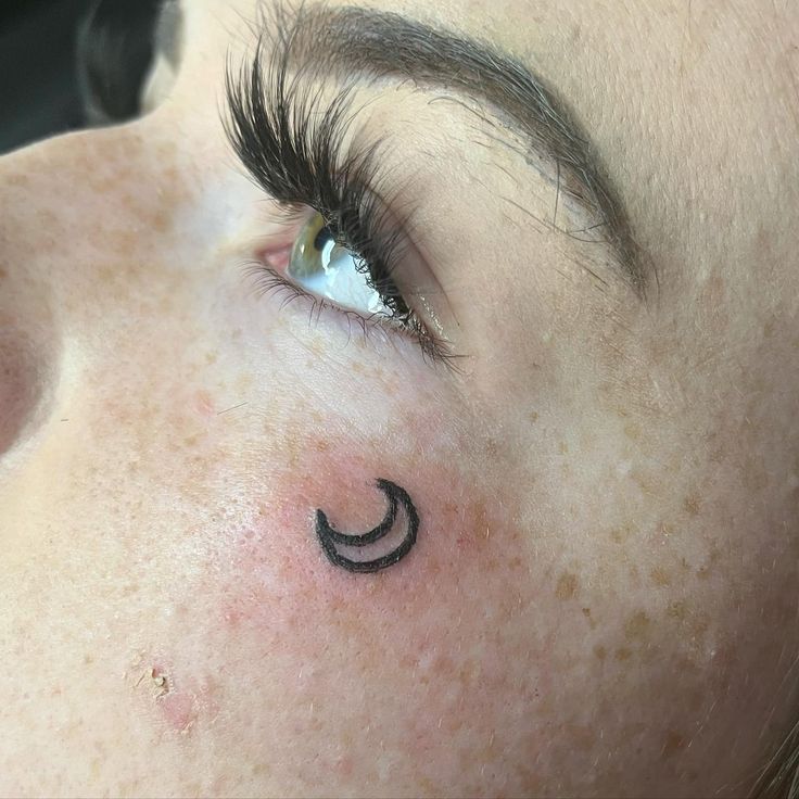 a woman's eye with a crescent tattoo on her forehead