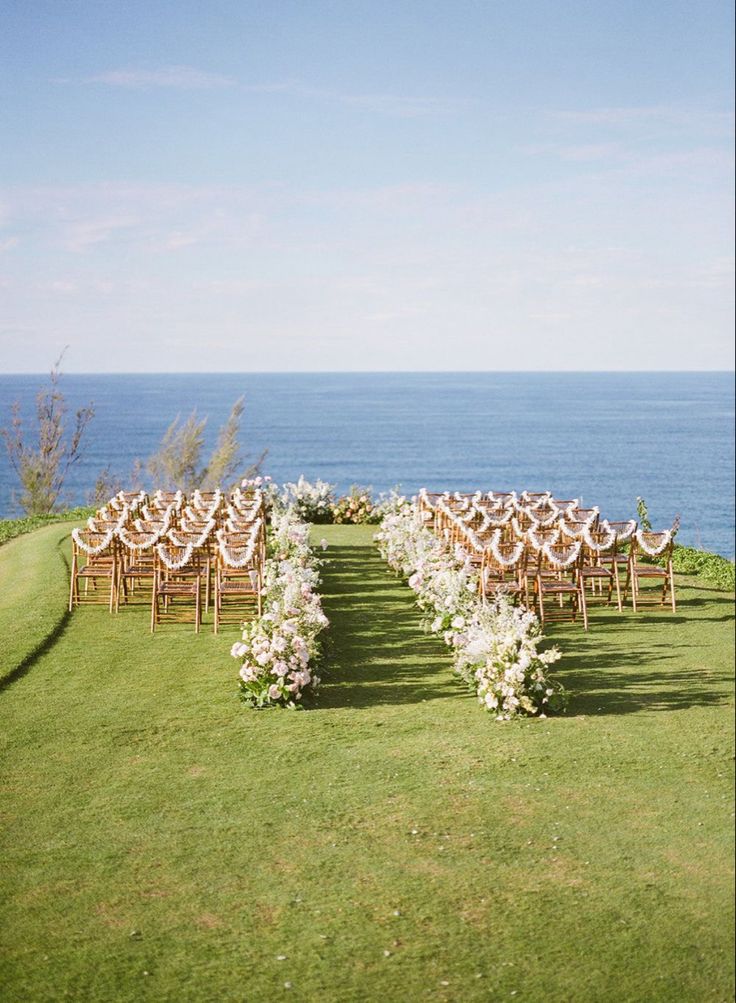 an outdoor ceremony set up with chairs and flowers on the grass by the water's edge