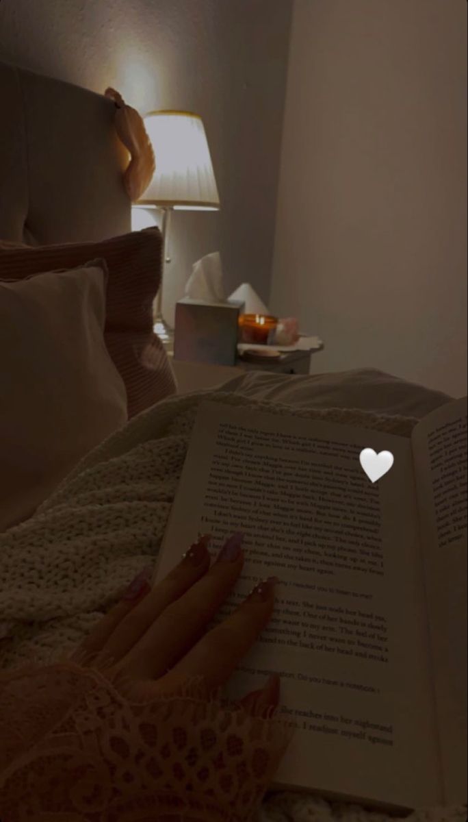 a person laying in bed reading a book with a heart shaped light on the page