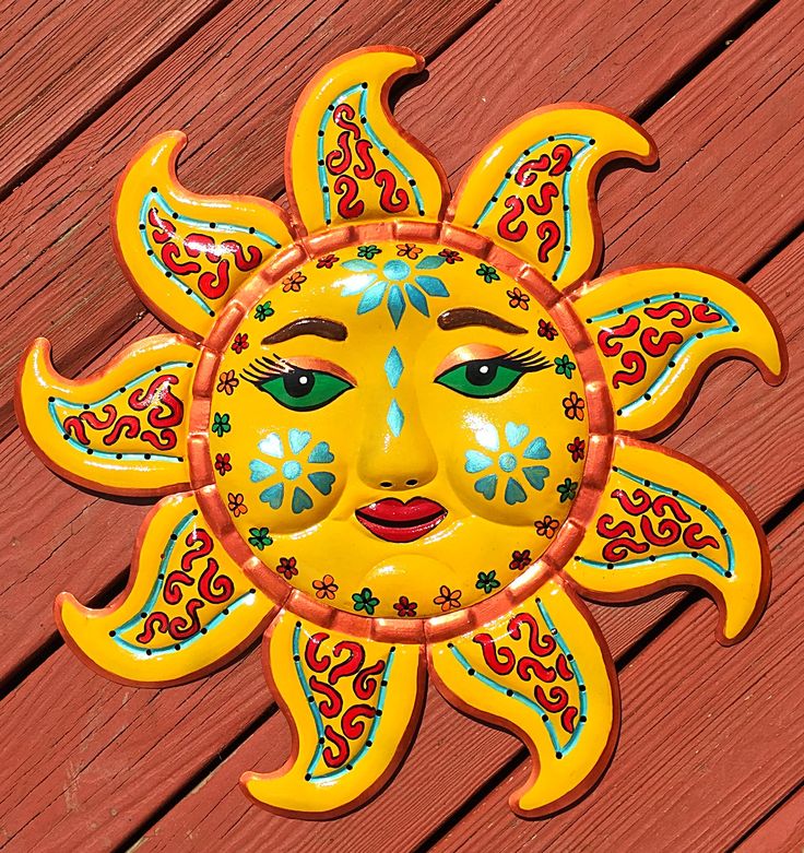 a yellow sun face on a red wooden surface with blue eyes and green, orange, and pink designs