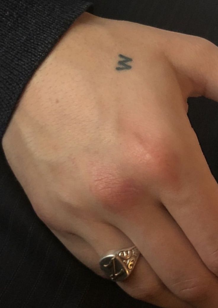 a person's hand with a ring on top of it and an arrow tattoo on the middle finger