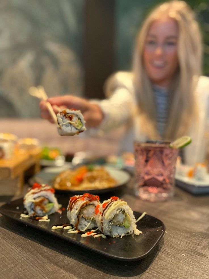 a woman eating sushi with chopsticks at a table in front of her