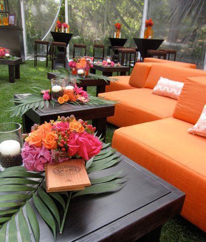 an orange couch sitting on top of a grass covered field next to tables and chairs