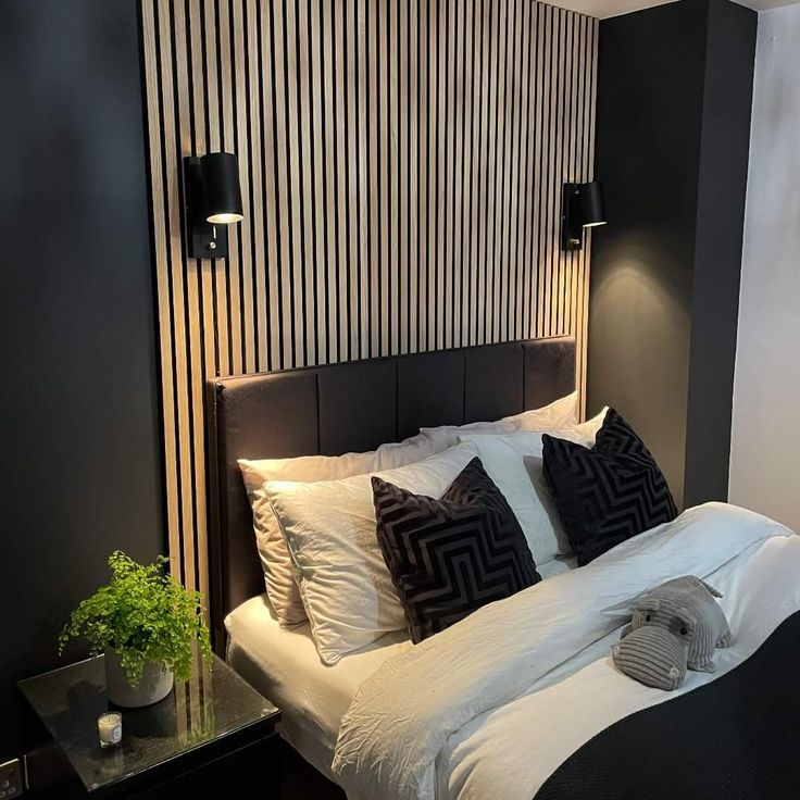 a bed with white sheets and black pillows in a room next to a wall mounted lamp