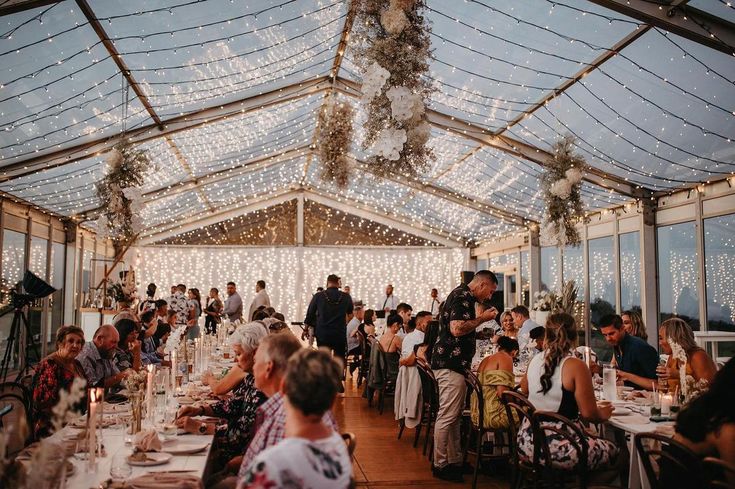 a large group of people sitting at tables in a room filled with glass walls and lights