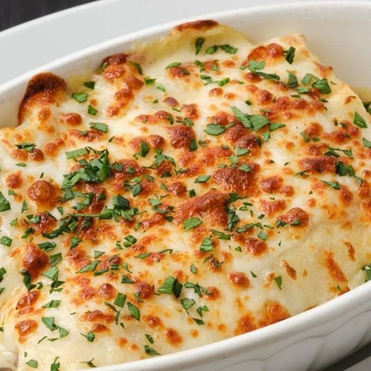 a casserole dish with cheese and herbs in it on a white platter