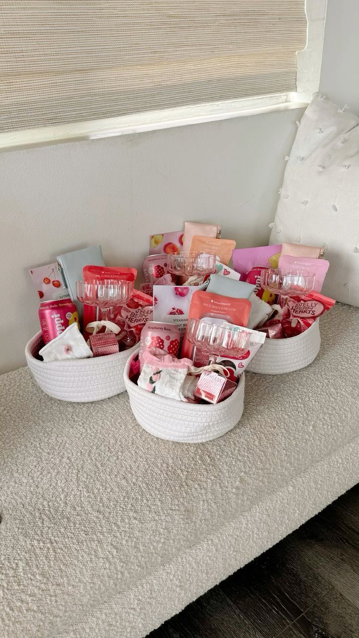 two baskets filled with pink and white items on a bed next to a window sill