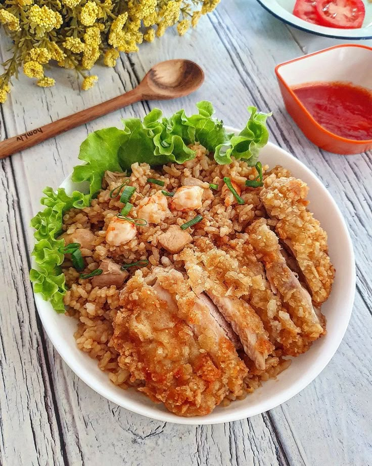 a white bowl filled with rice covered in meat and veggies next to sauce