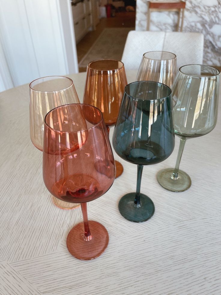 four wine glasses sitting on top of a table next to each other in different colors