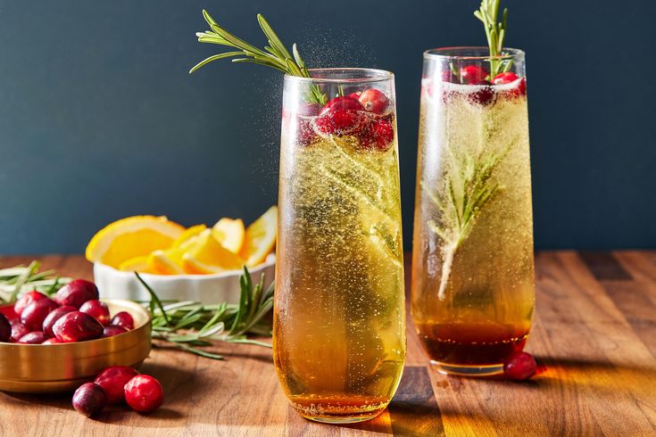 two glasses filled with liquid and garnish next to bowls of cranberries