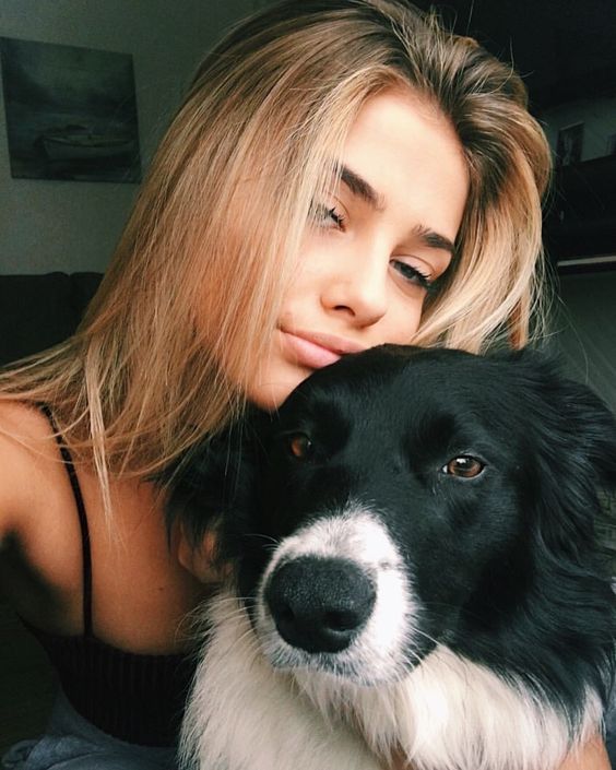 a woman is cuddling her dog's face while she looks at the camera