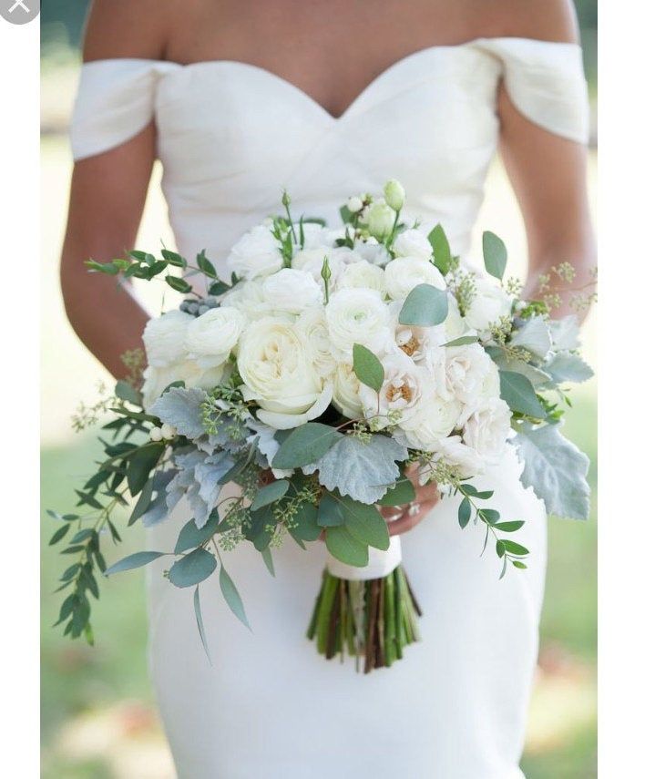 a bride holding a bouquet of white flowers and greenery on her wedding day at the park