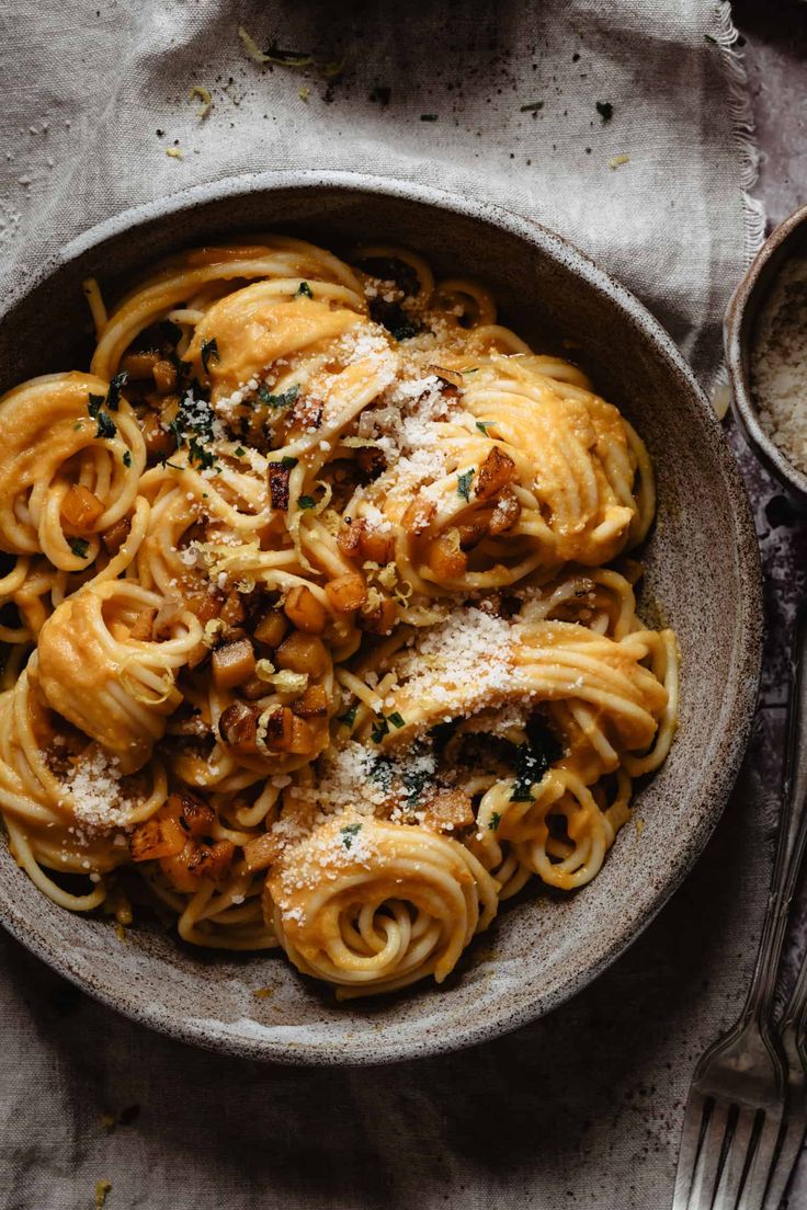 a bowl filled with pasta and sauce on top of a table next to silverware