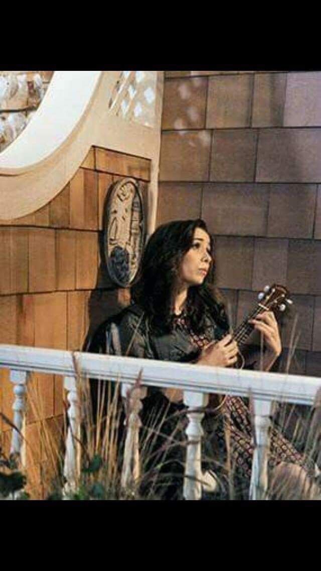 a woman sitting on top of a wooden bench next to a building holding a guitar