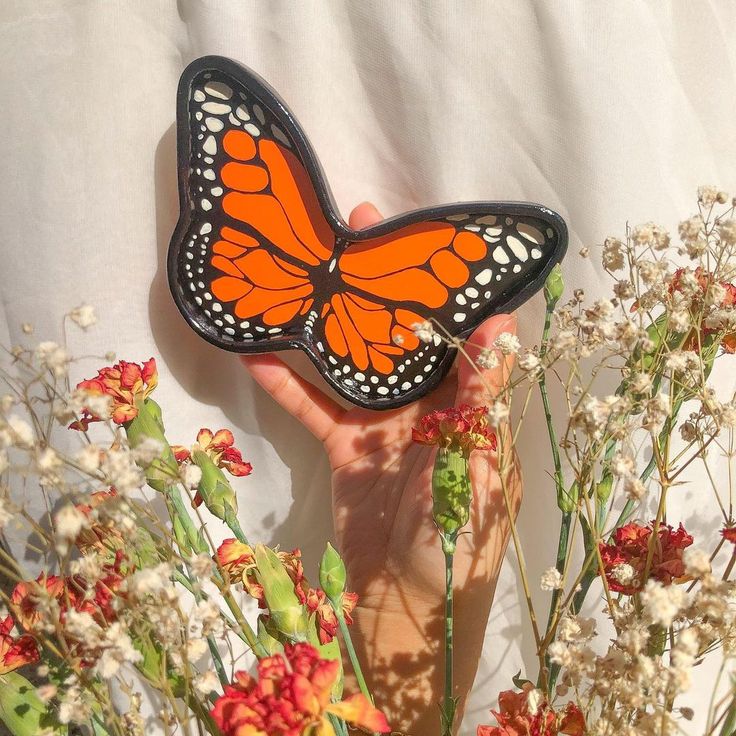 a person holding a butterfly in their hand near some flowers and other wildflowers