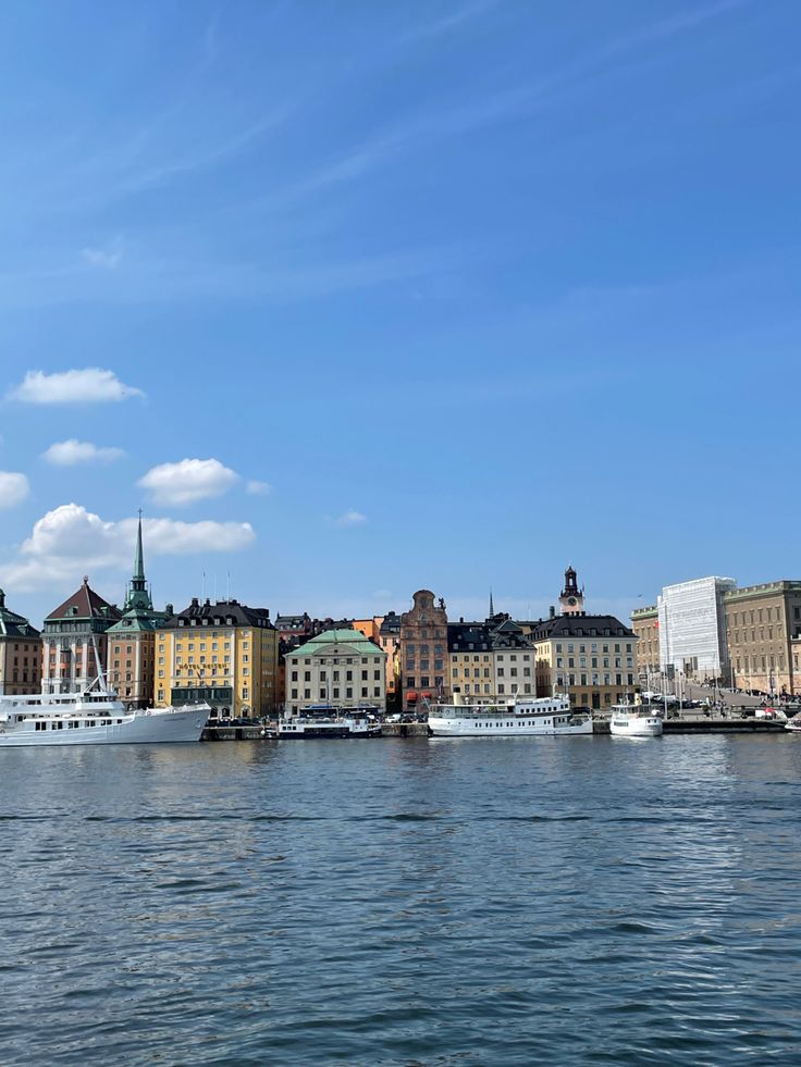 boats are docked in the water next to some buildings and blue sky with wispy clouds