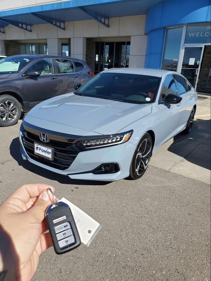 a person holding a car key in front of a honda dealership with other cars