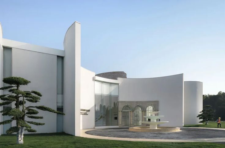 a white building with trees in front of it and people walking around the outside area