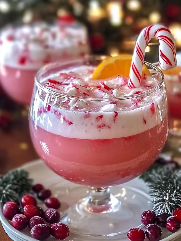 two glasses filled with red and white drink on top of a plate next to candy canes