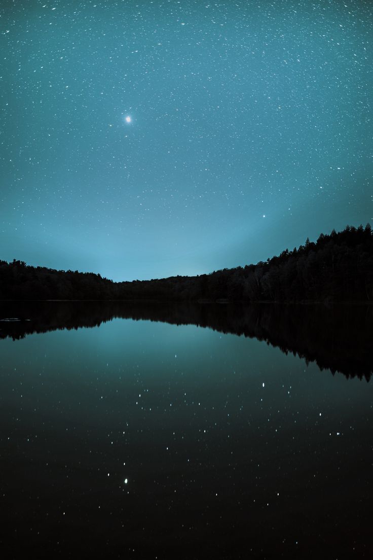 the night sky is reflected in water with trees on both sides and stars above it