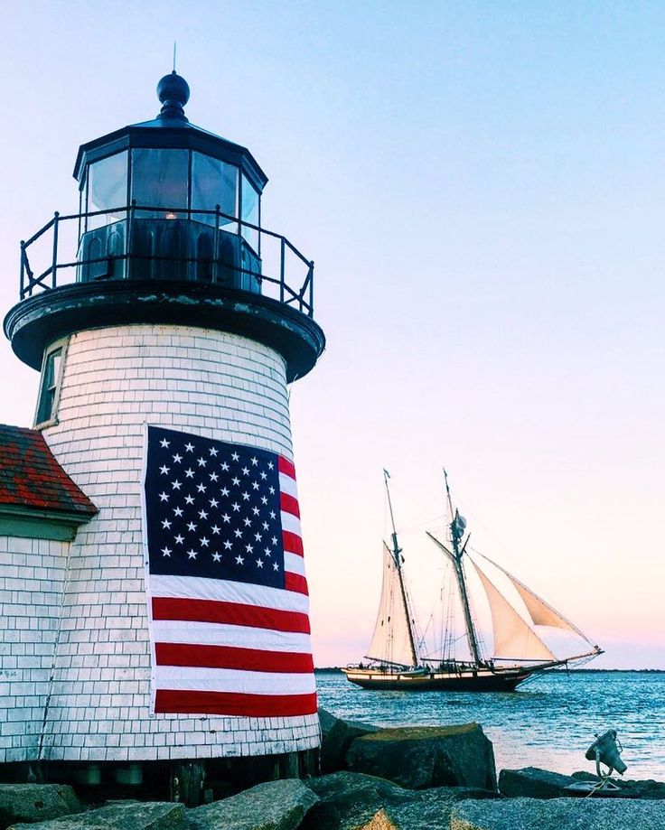 a lighthouse with an american flag painted on it next to the ocean and a sailboat