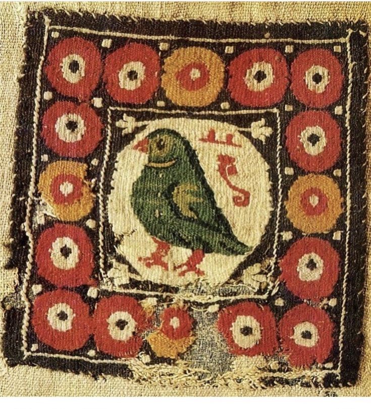 an embroidered piece with a green bird on it's back and red flowers around the edges