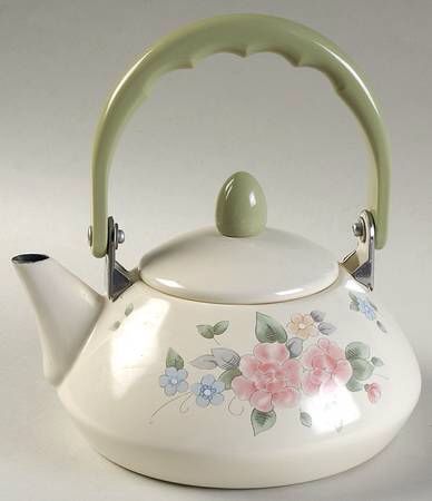 a white tea kettle with flowers painted on the side and a green handle is shown