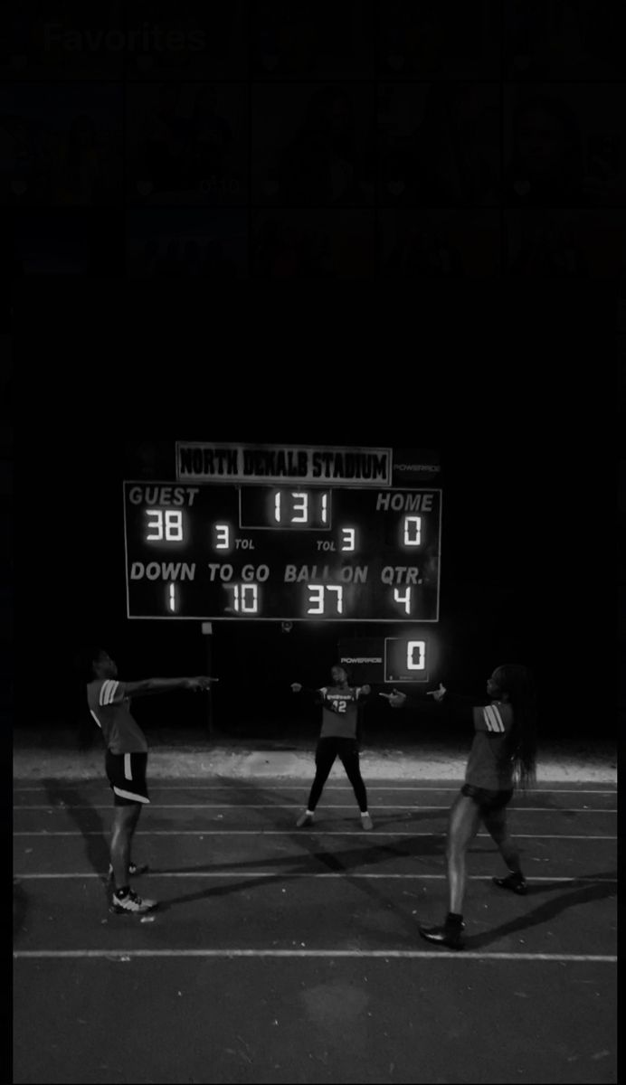 three people standing in front of an electronic scoreboard on a tennis court at night