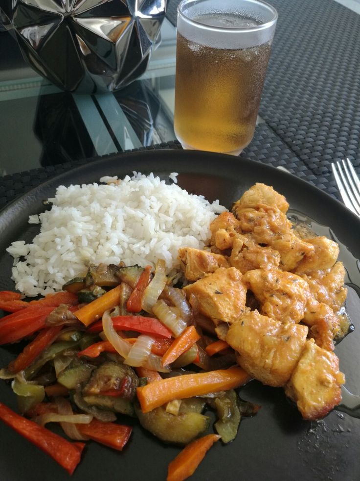 a black plate topped with rice and veggies next to a glass of beer